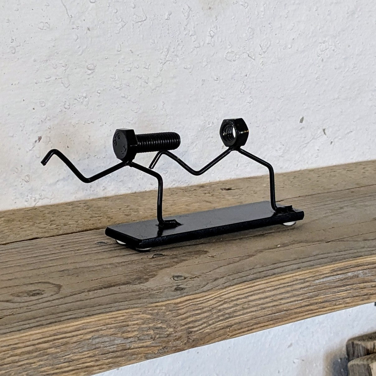 Skulpturen er lavet af møtrikker, bolte og stål. Den er malet sort.