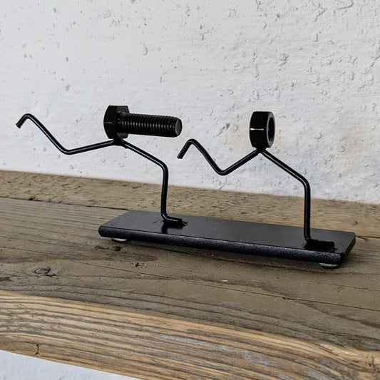 Skulpturen er lavet af møtrikker, bolte og stål. Den er malet sort.