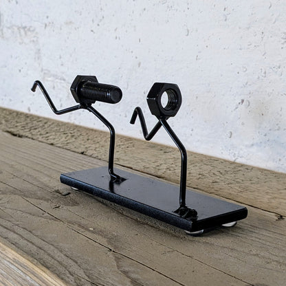 Skulpturen er lavet af møtrikker, bolte og stål. Den er malet sort.