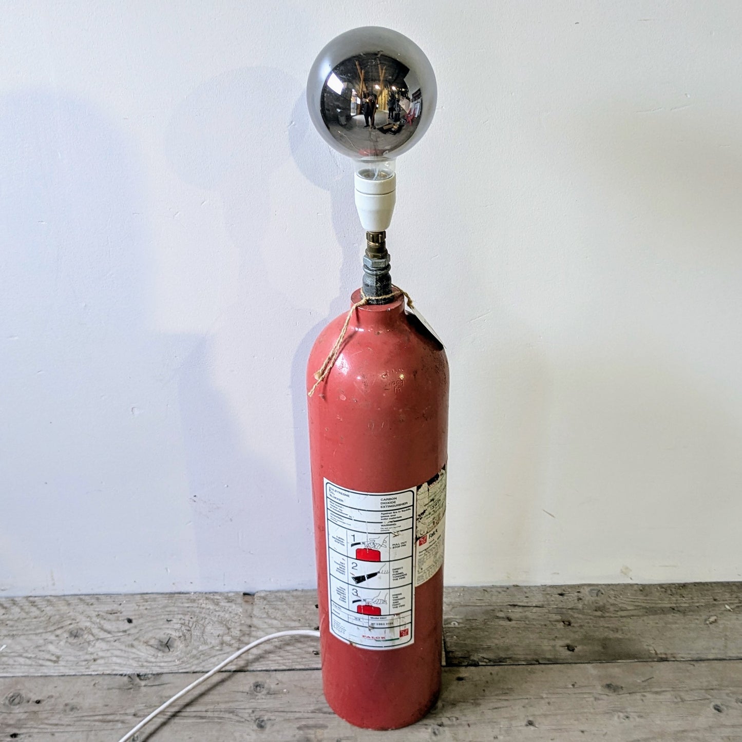Her ses lampen er lavet af en gammel Falck pulverslukker i metal, som er blevet opcyclet til en gulvlampe.