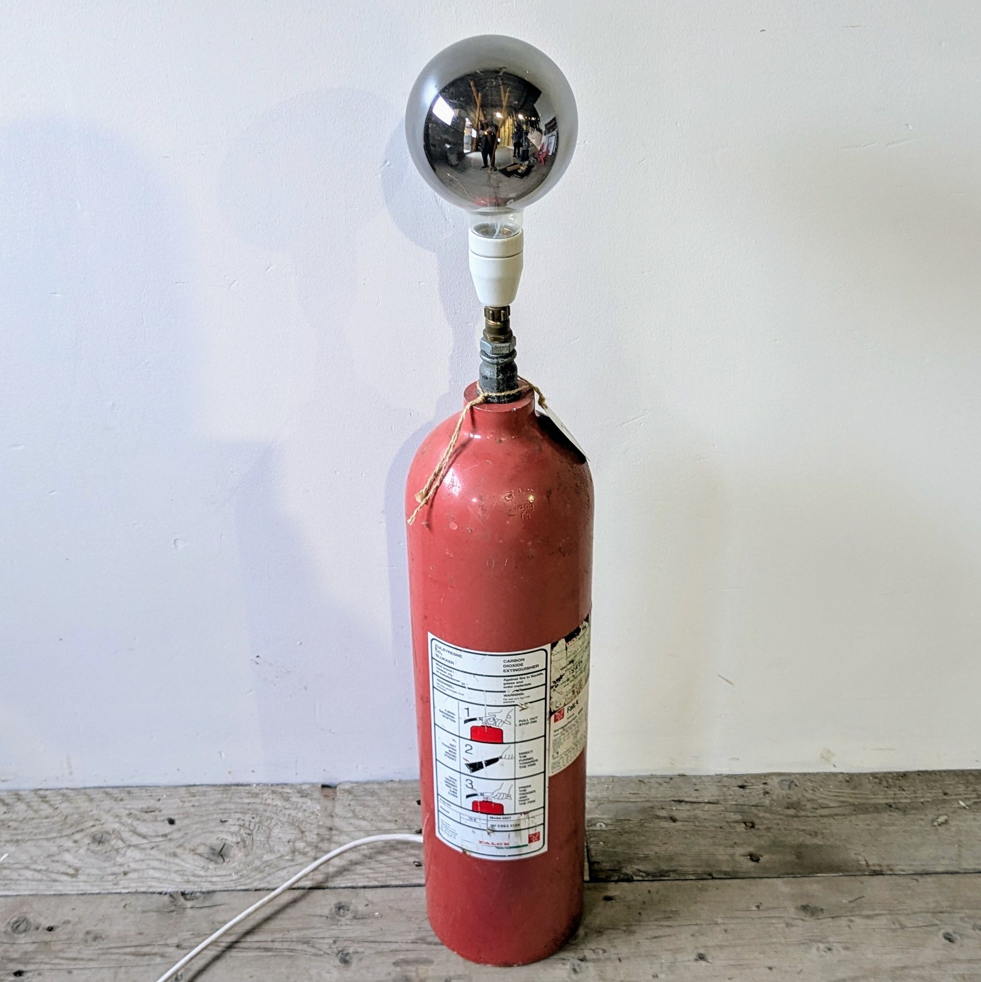 Her ses lampen er lavet af en gammel Falck pulverslukker i metal, som er blevet opcyclet til en gulvlampe.