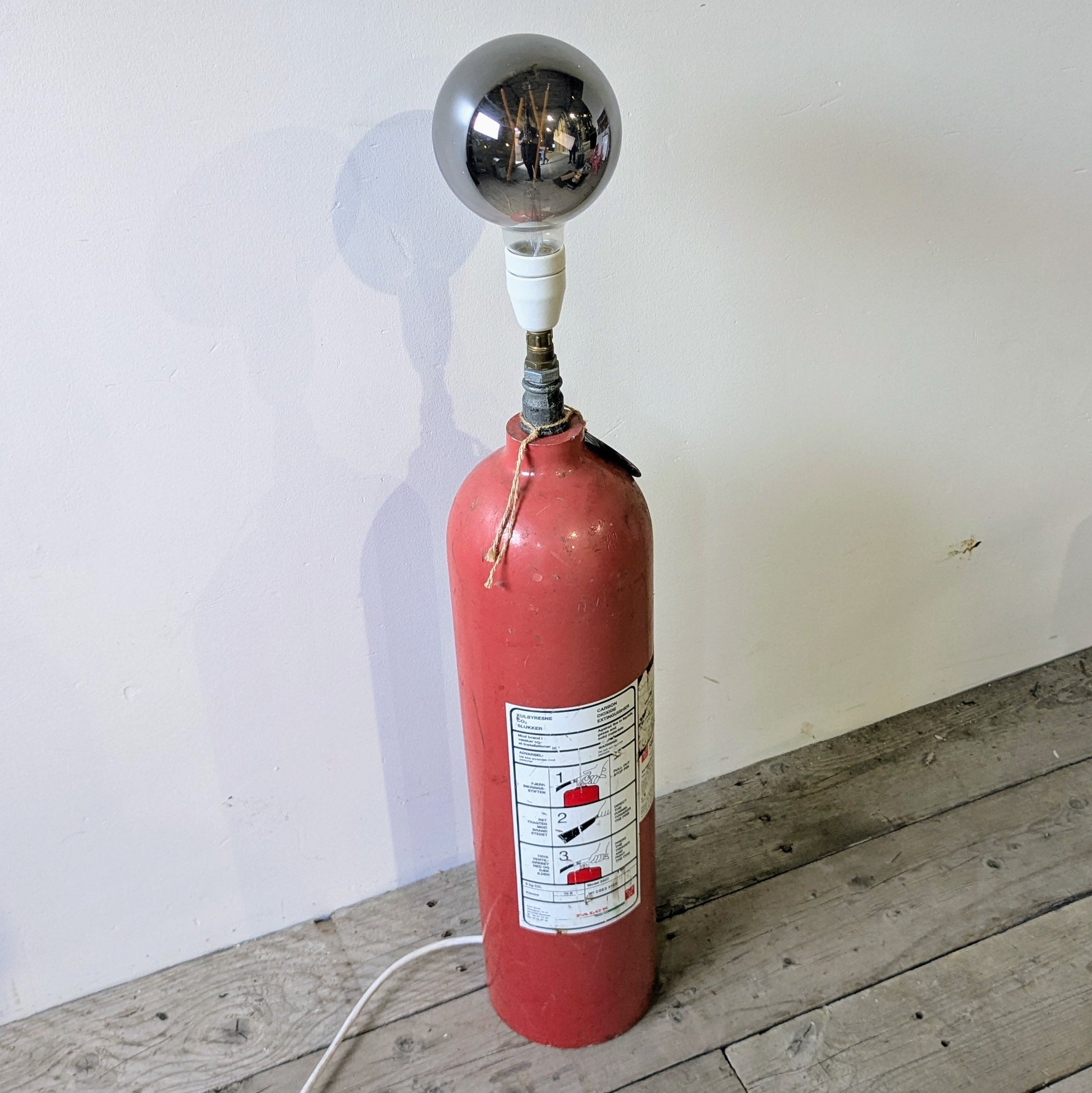 Her ses lampen er lavet af en gammel Falck pulverslukker i metal, som er blevet opcyclet til en gulvlampe.